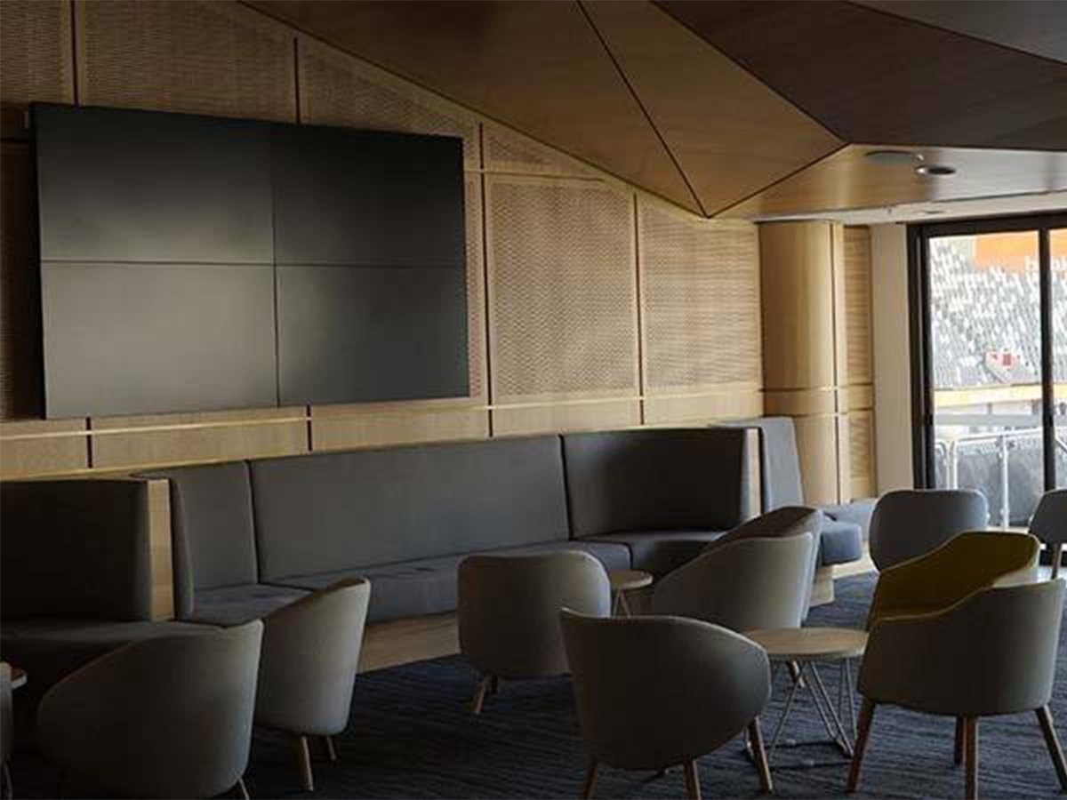 Contemporary lounge area with cushioned chairs, a wall-mounted screen, and natural light from glass doors.