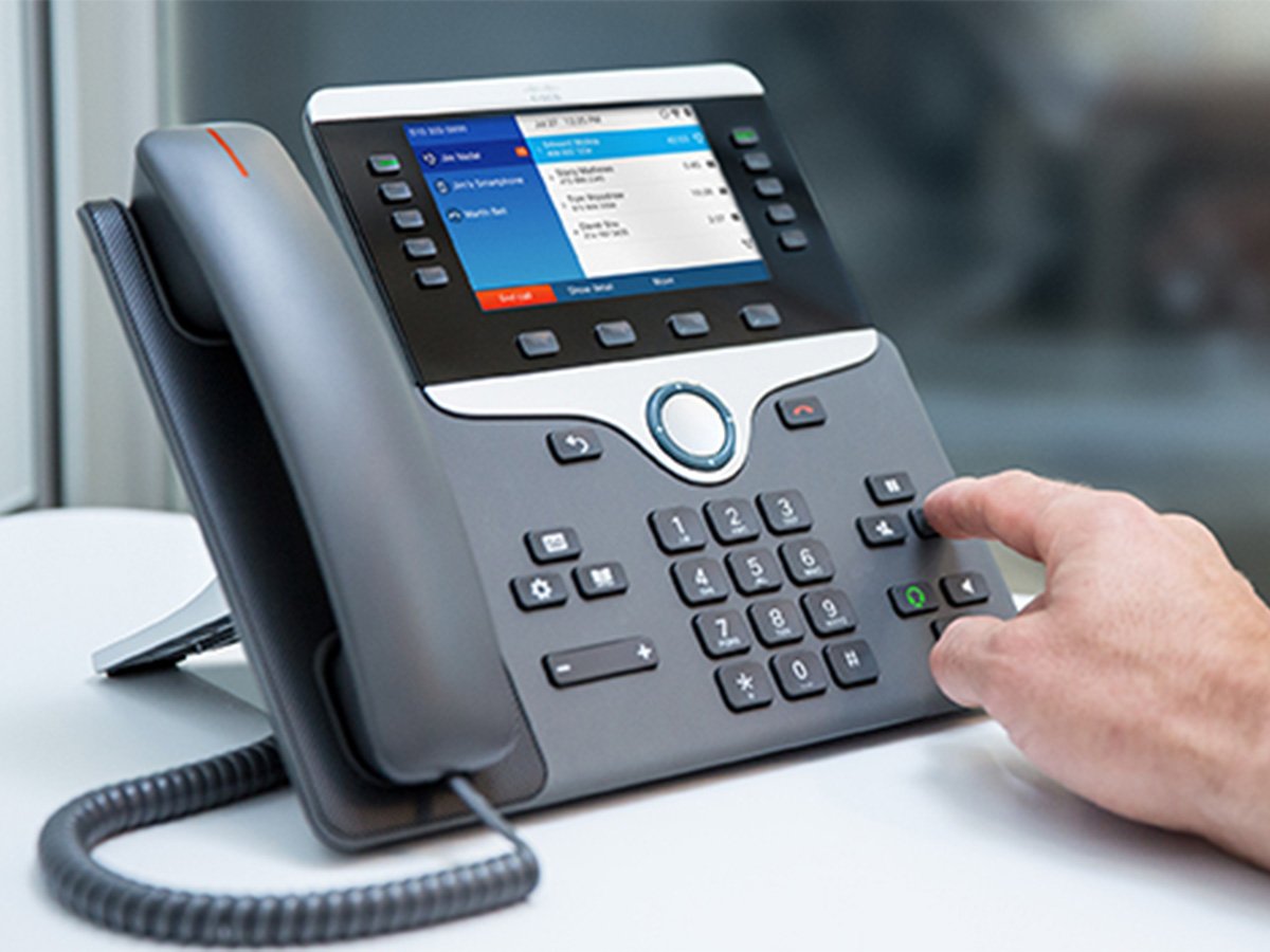 Person pressing buttons on a Cisco office desk phone with a digital display showing call options.