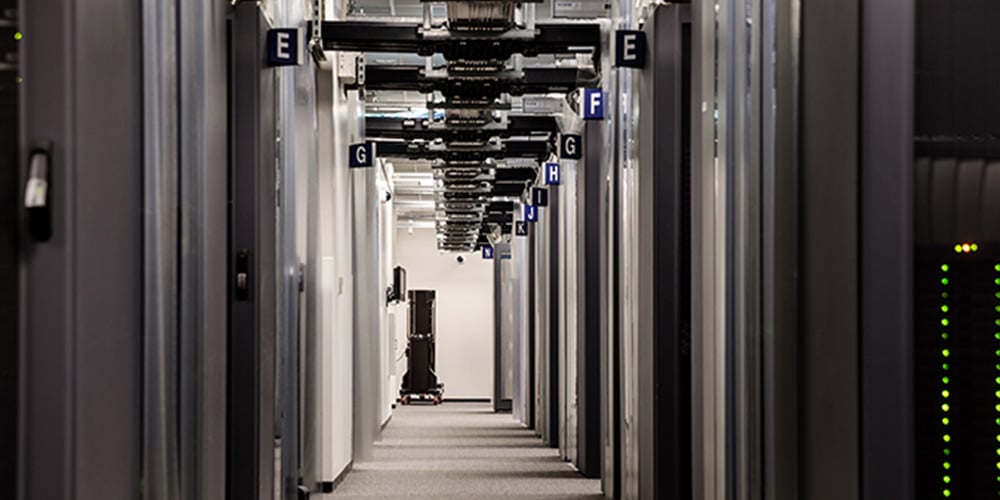 Long hallway in a data center with labeled sections and overhead cable trays for structured wiring.