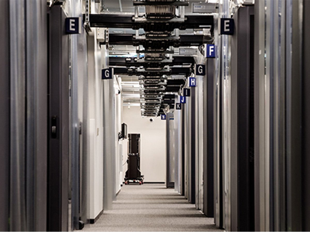 Long hallway in a data center with labeled sections and overhead cable trays for structured wiring.