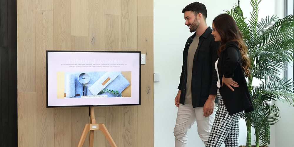 Two people viewing a digital display on a stand in a modern office environment.