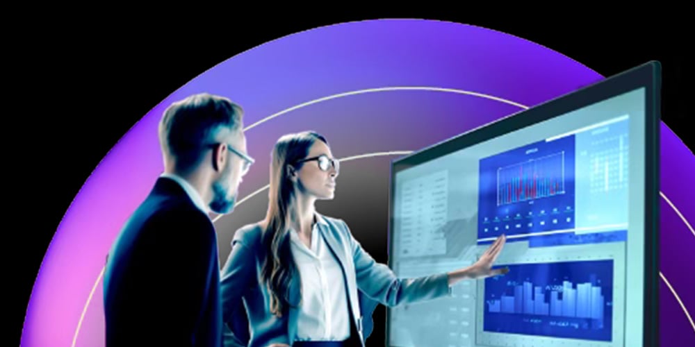 Two professionals reviewing analytics and charts on a large interactive display in a modern workspace.