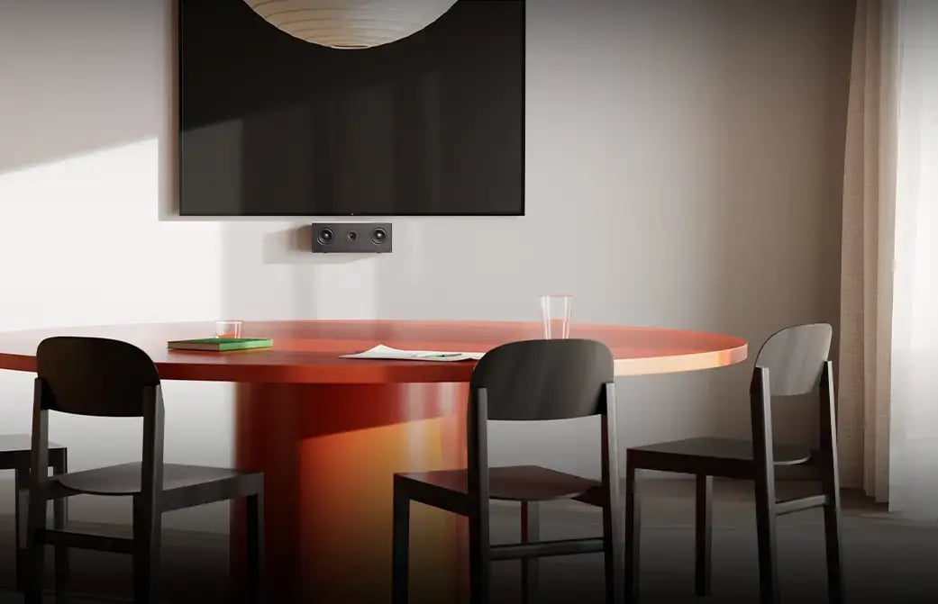 Meeting room with a round table, chairs, wall display, and a small conference camera below the screen.