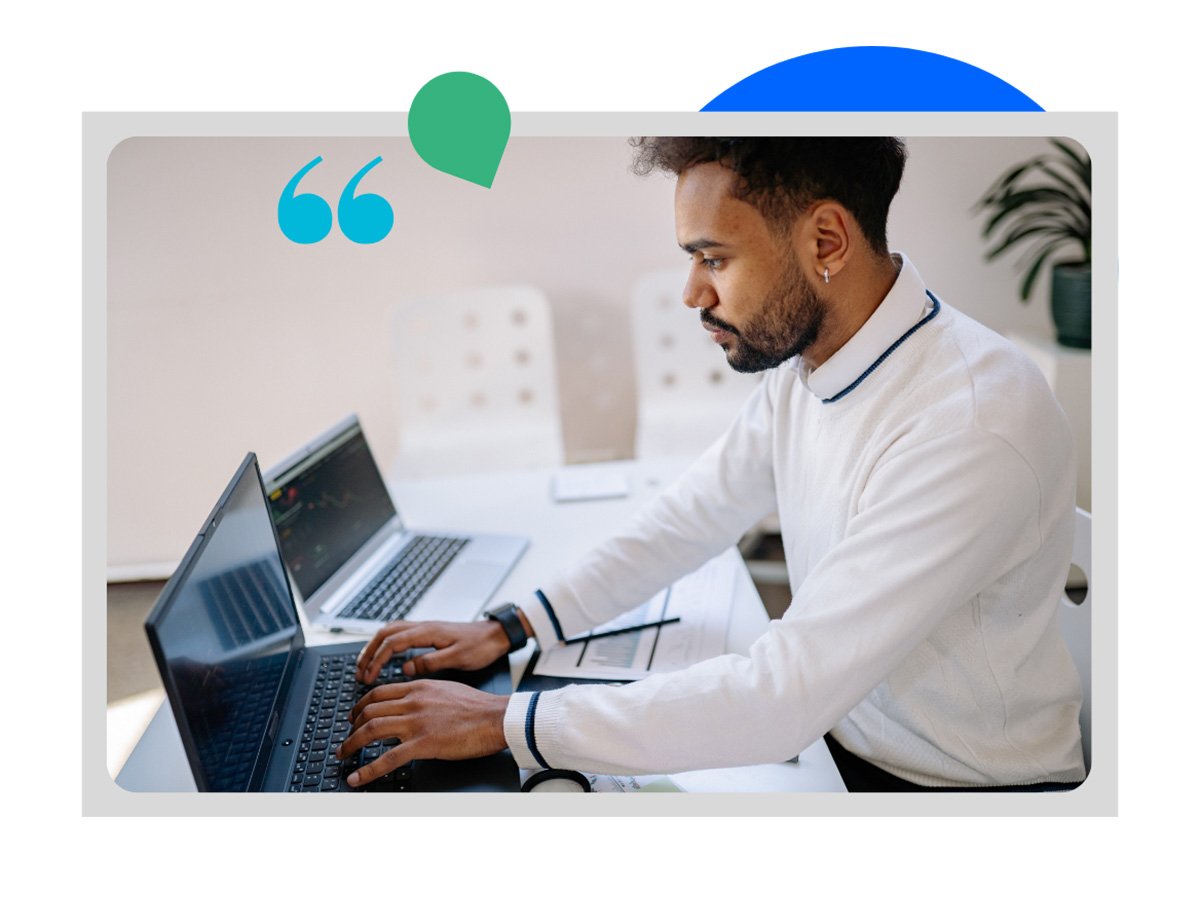 Person working on a laptop at a desk with a second laptop and workspace items nearby.