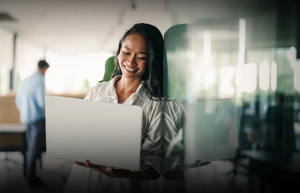 Person standing in an office using a laptop near a glass wall.