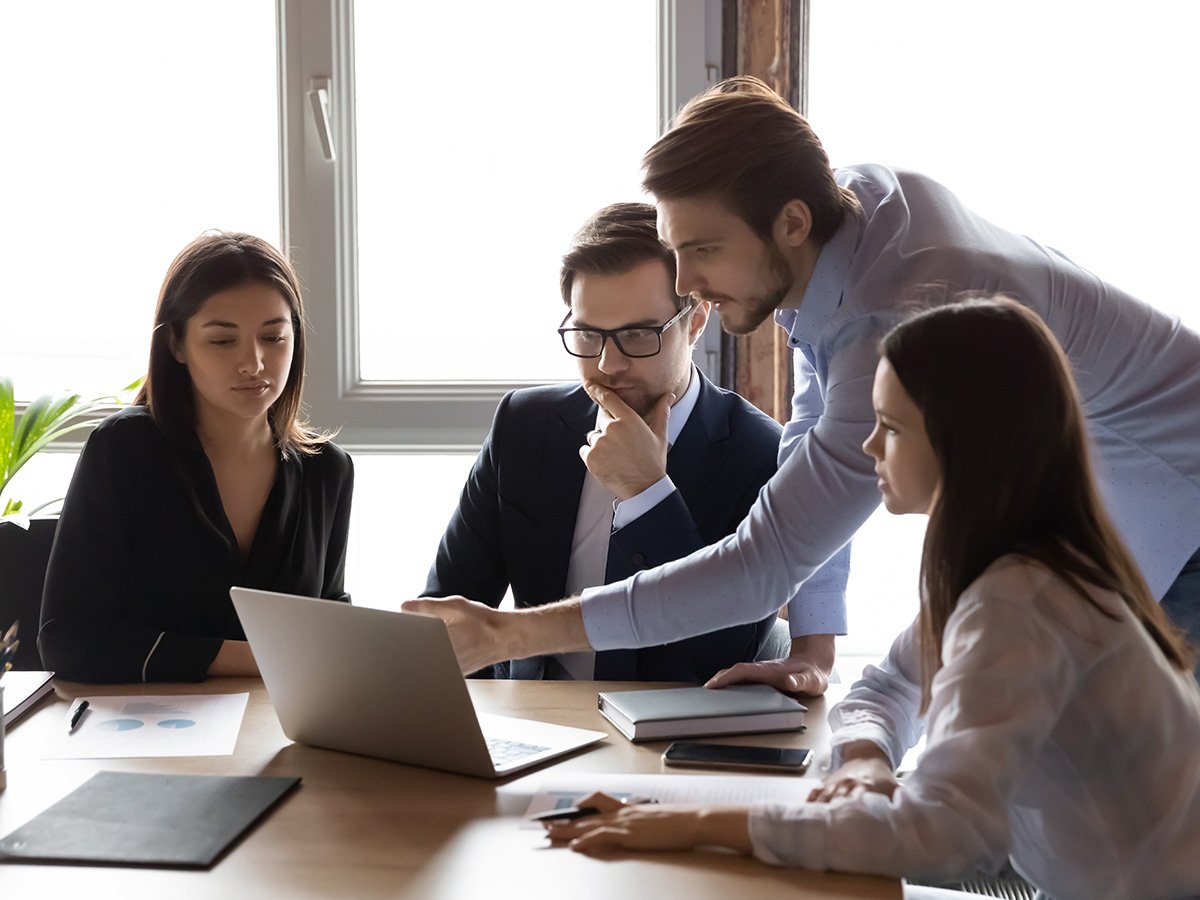 Small team gathered around a laptop discussing content displayed on the screen.