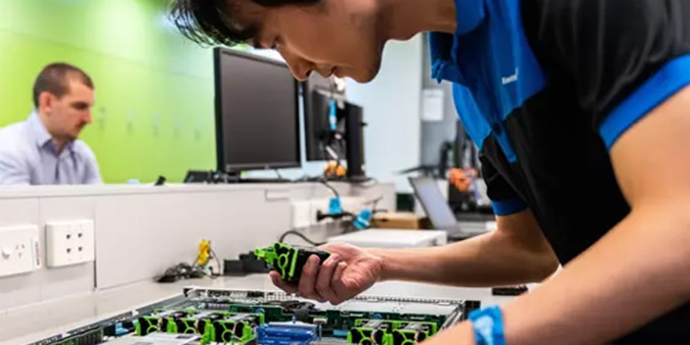 Technician holding an electronic device while testing or inspecting equipment in a laboratory environment.