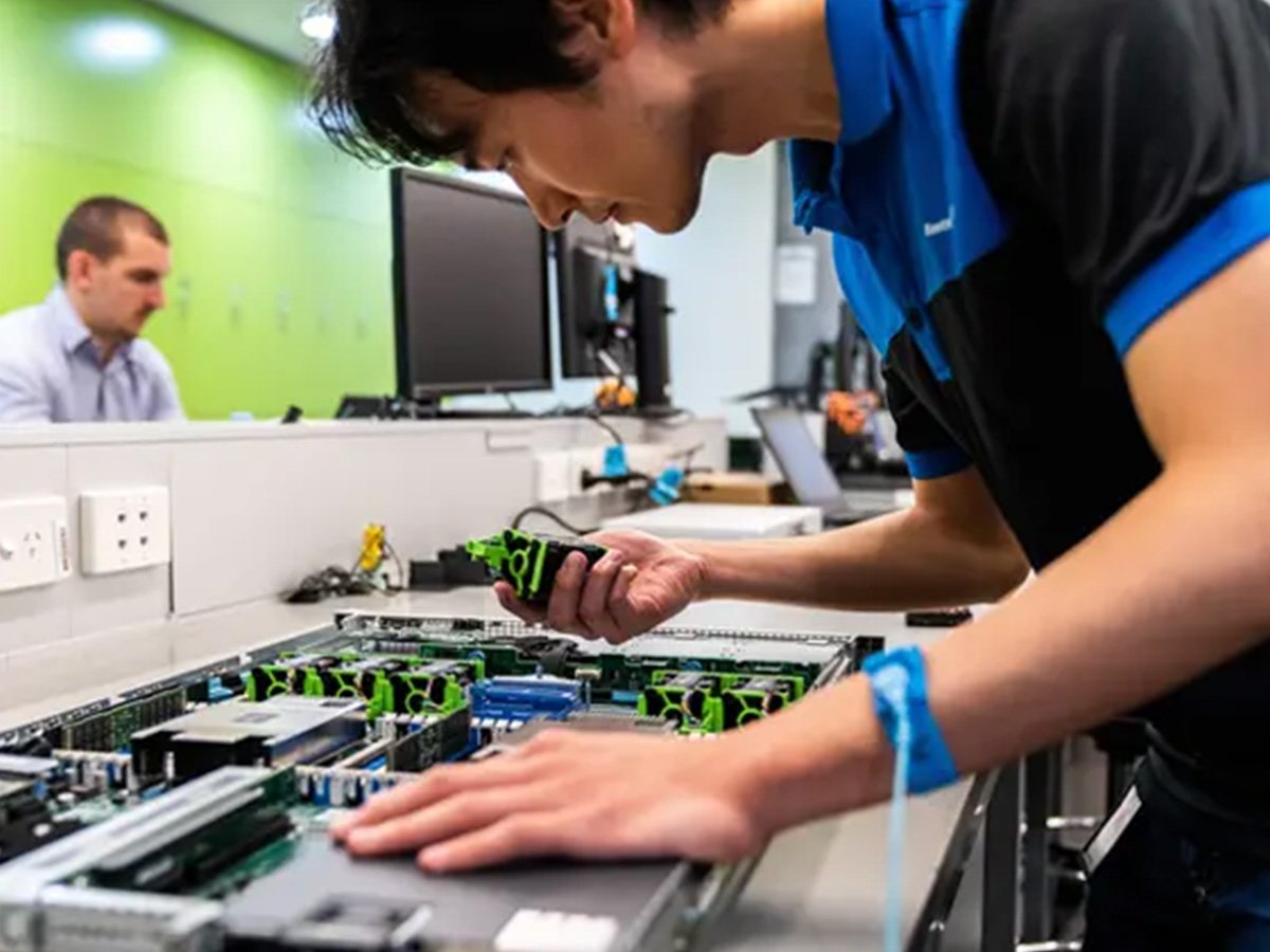 Technician holding an electronic device while testing or inspecting equipment in a laboratory environment.
