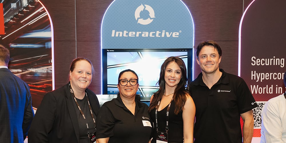 Team members standing together at a technology event booth with branded display screens behind them.