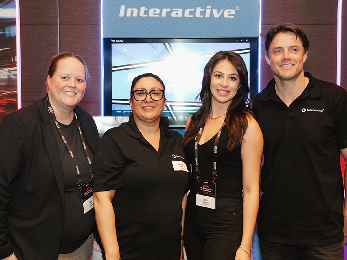 Team members standing together at a technology event booth with branded display screens behind them.