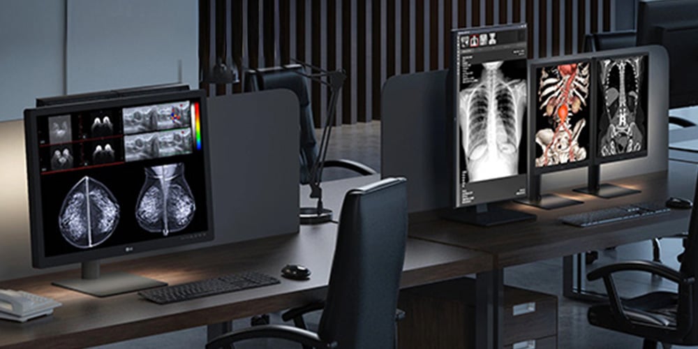Modern office with multiple computer monitors displaying grayscale and color medical scans, including X-rays and MRIs, on a wooden desk.