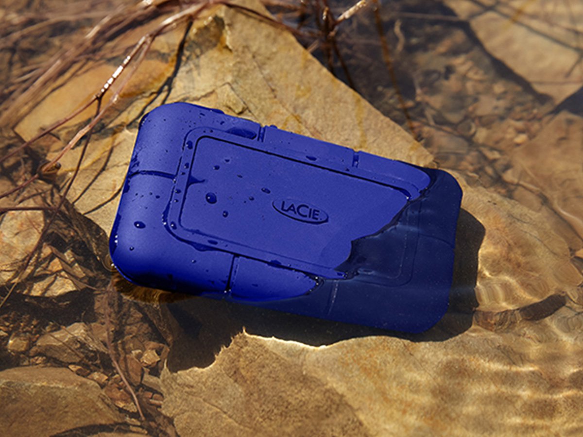Blue LaCie rugged hard drive partially submerged in shallow water.