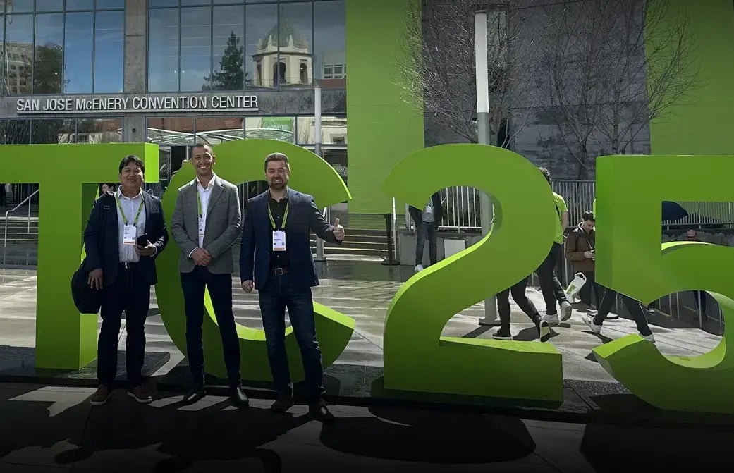 Three people standing in front of large green event letters outside a convention center.