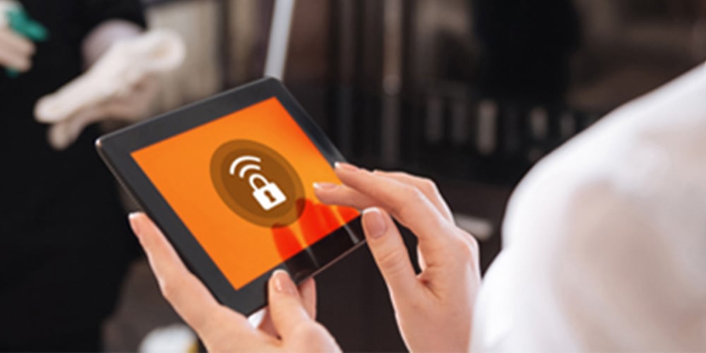 Person holding a tablet showing a wireless lock icon while staff work in the background.