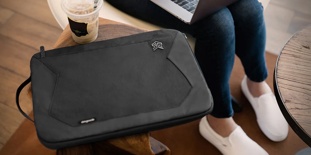 Black laptop sleeve placed on a wooden table next to a drink.