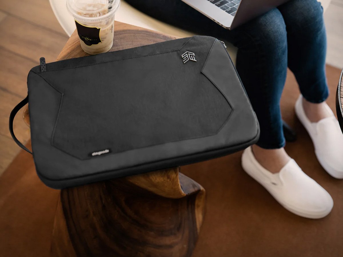 Black laptop sleeve placed on a wooden table next to a drink.