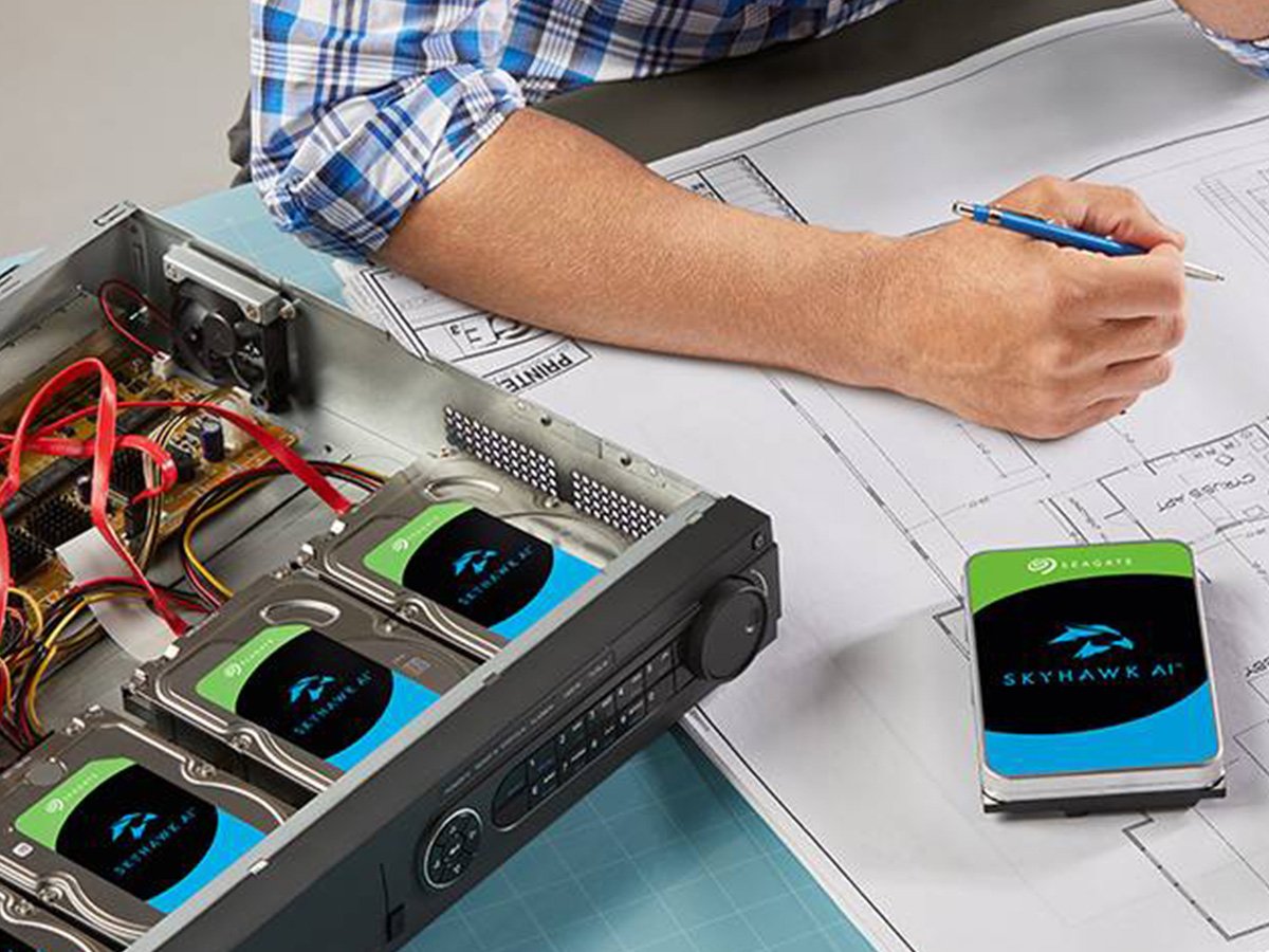 Open storage chassis with multiple hard drives beside technical drawings on a work desk.