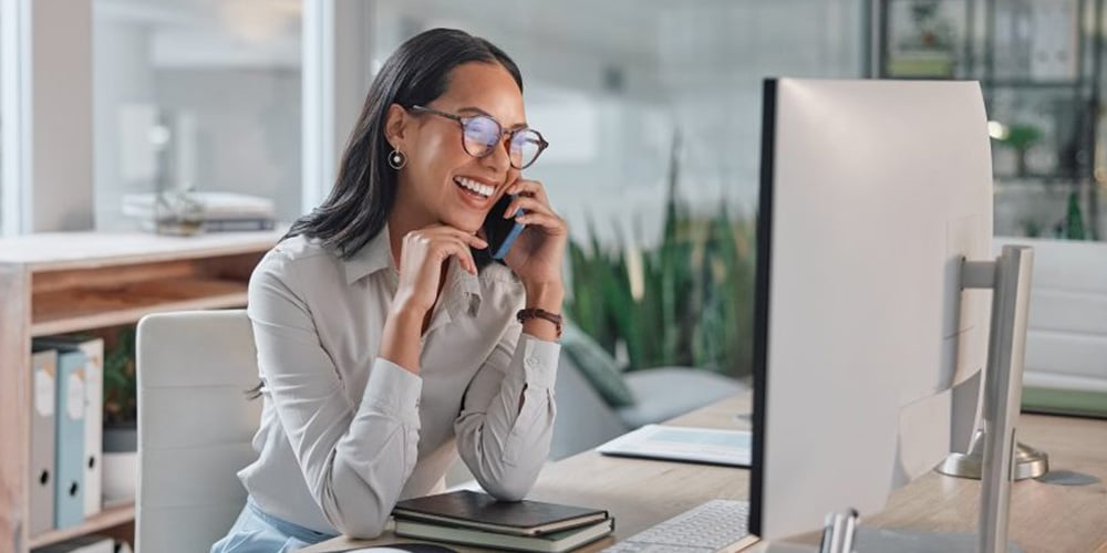 Person seated at a desk, looking at a computer monitor in a bright, modern workspace.