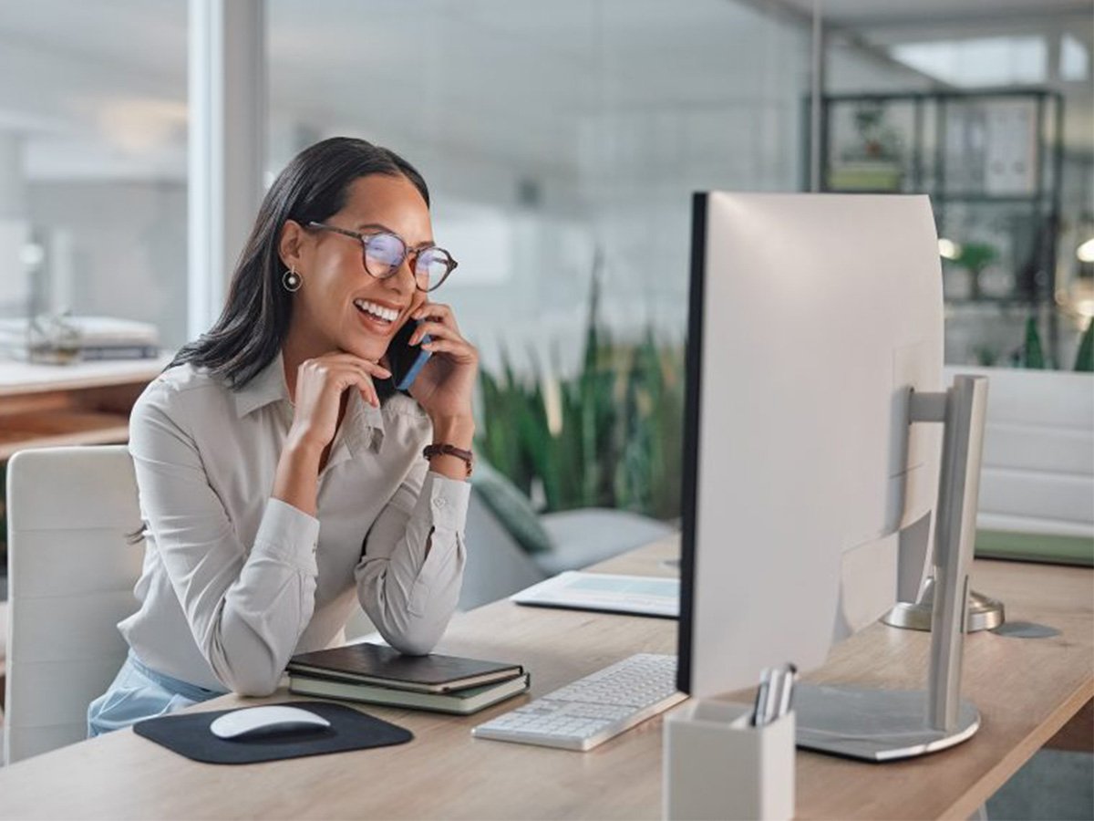 Person seated at a desk, looking at a computer monitor in a bright, modern workspace.
