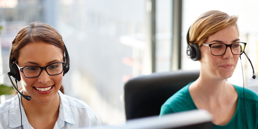 Two customer support staff wearing headsets and working at computer monitors.