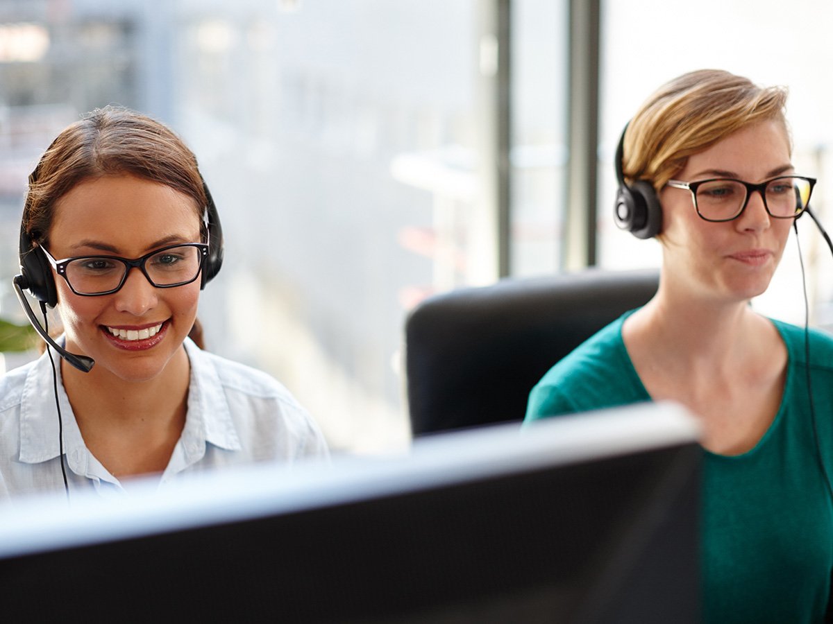 Two customer support staff wearing headsets and working at computer monitors.