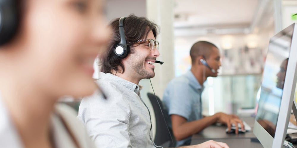 People working at desktop computers in an open-plan office environment.