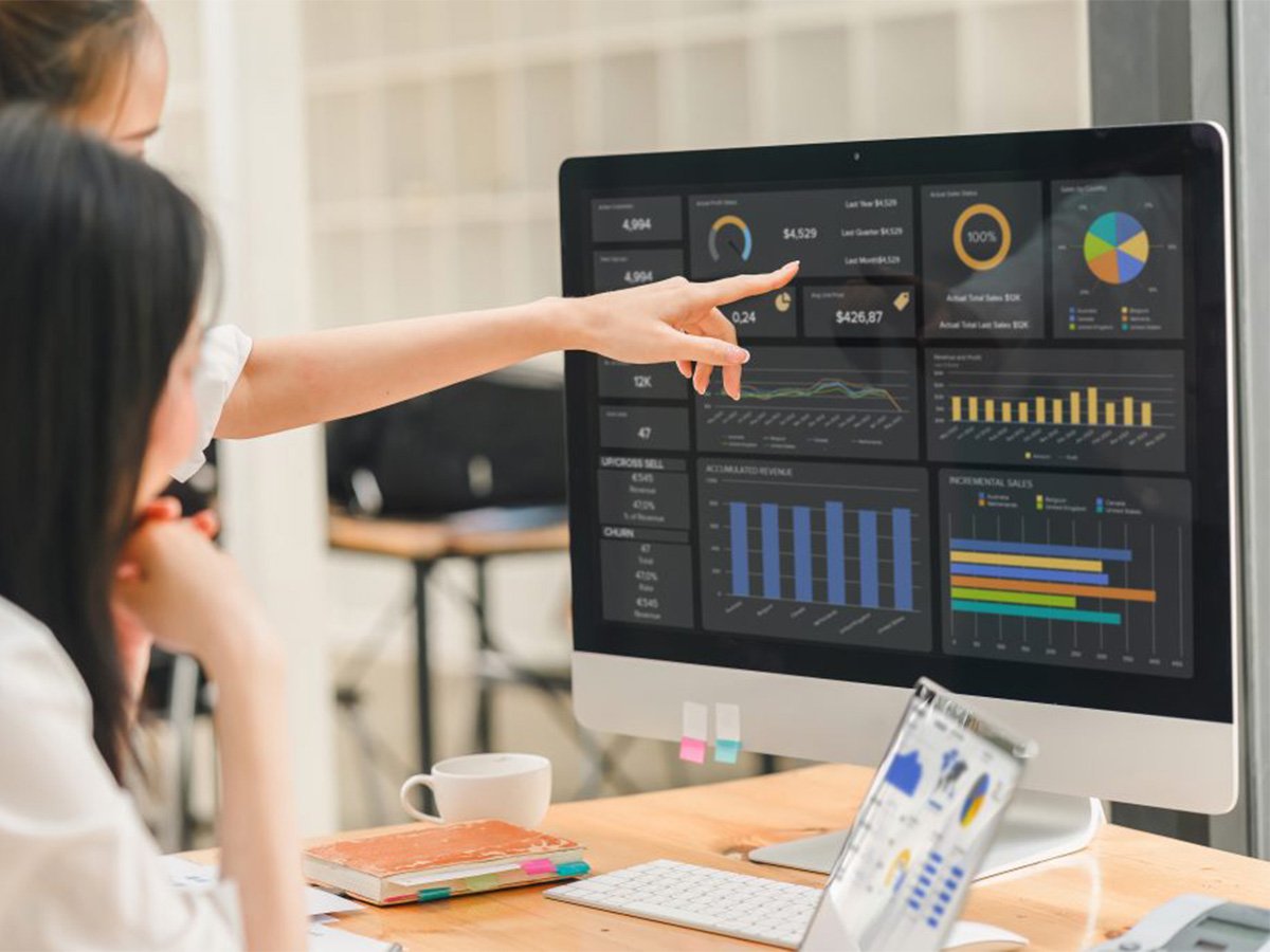 Person pointing at data dashboards on a large desktop monitor in a modern office.