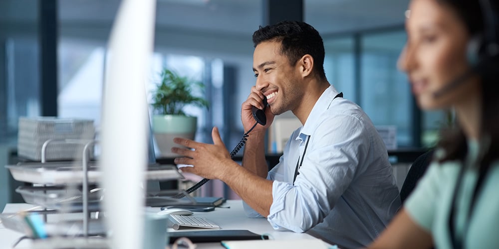 Person talking on the phone while sitting at an office desk infront of computer