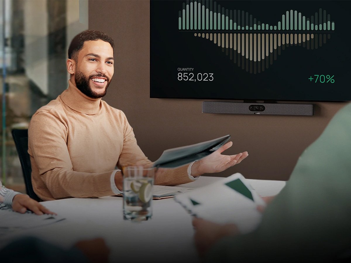 Colleagues in a meeting as one person presents data on a wall-mounted screen showing charts and growth figures.