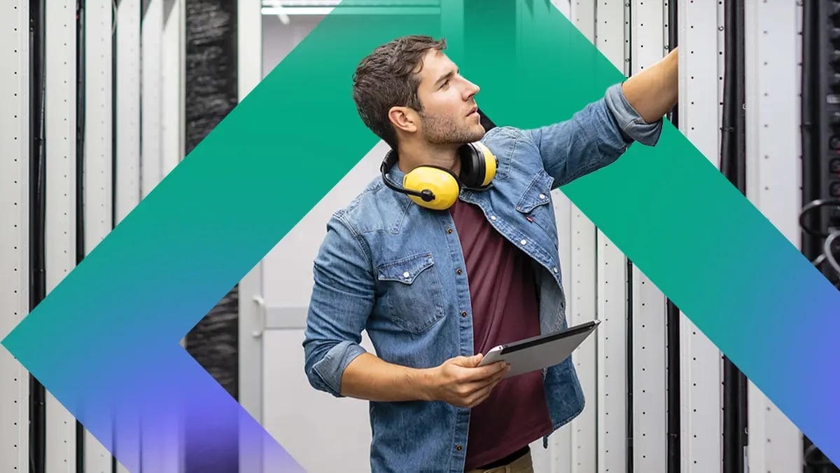 A technician works in a server room, holding a tablet and adjusting equipment racks.
