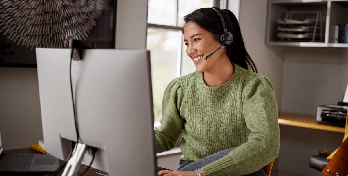 Person wearing a Jabra headset while working at a desktop computer in a home office.