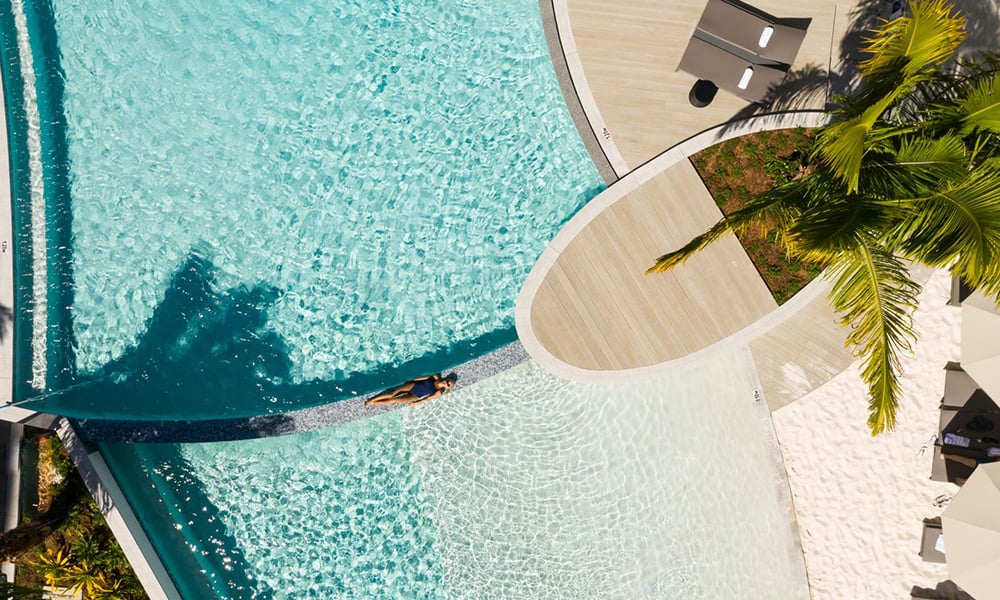 Aerial view of a resort pool with palm trees and a swimmer.
