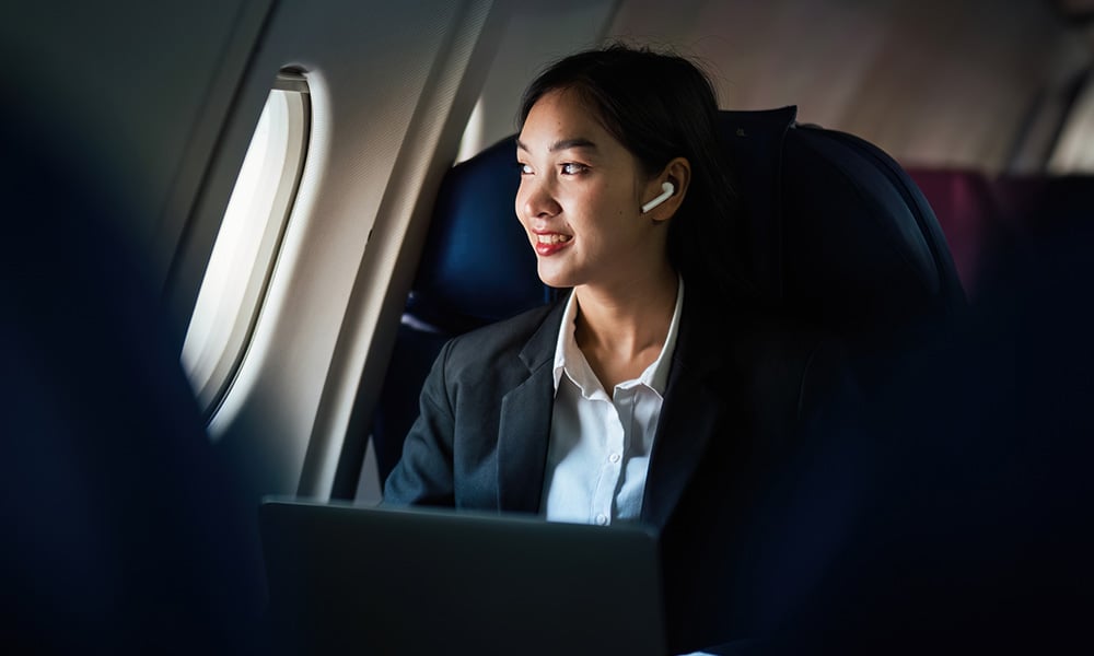 Person working on a laptop while seated by an airplane window.