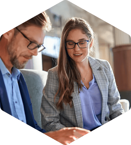 Two professionals wearing glasses review content on a laptop together in an office setting.