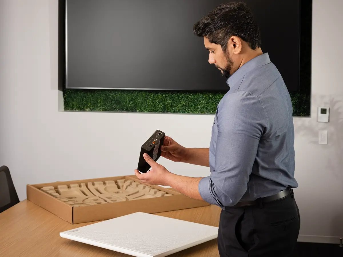 A person examining an electronic device component on a table with unpacked equipment nearby.