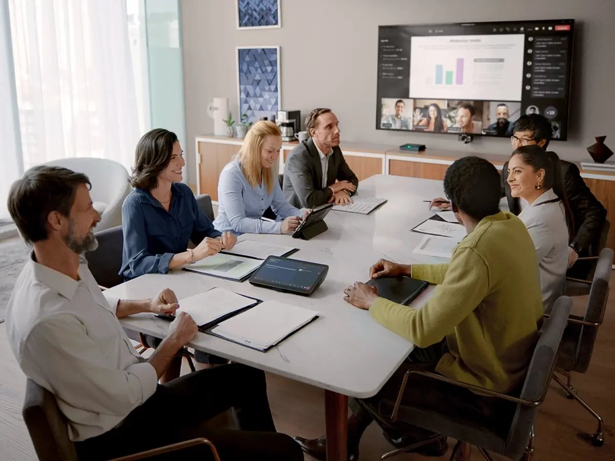 Business meeting with a diverse team seated around a conference table, reviewing documents and a presentation displayed on a screen.