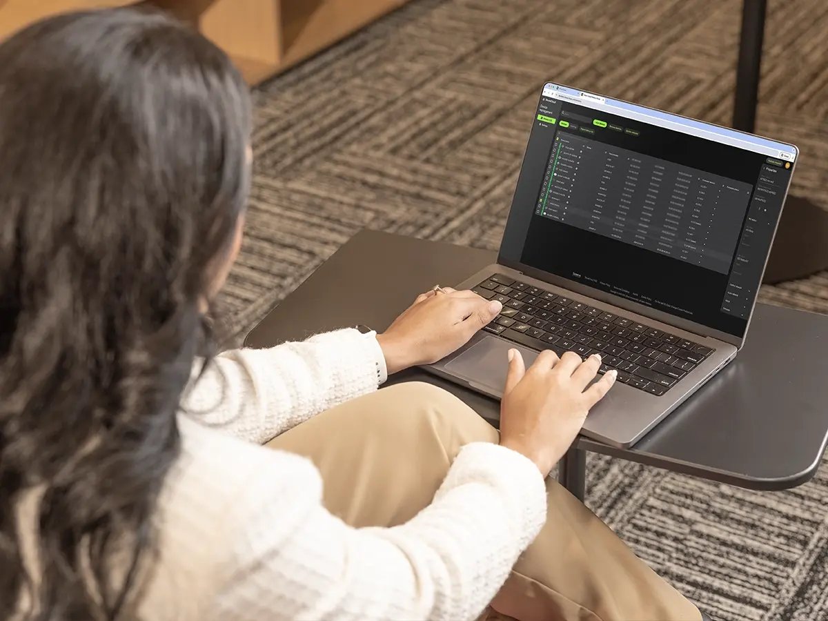 A person sitting at a small desk working on a laptop displaying a device management dashboard.
