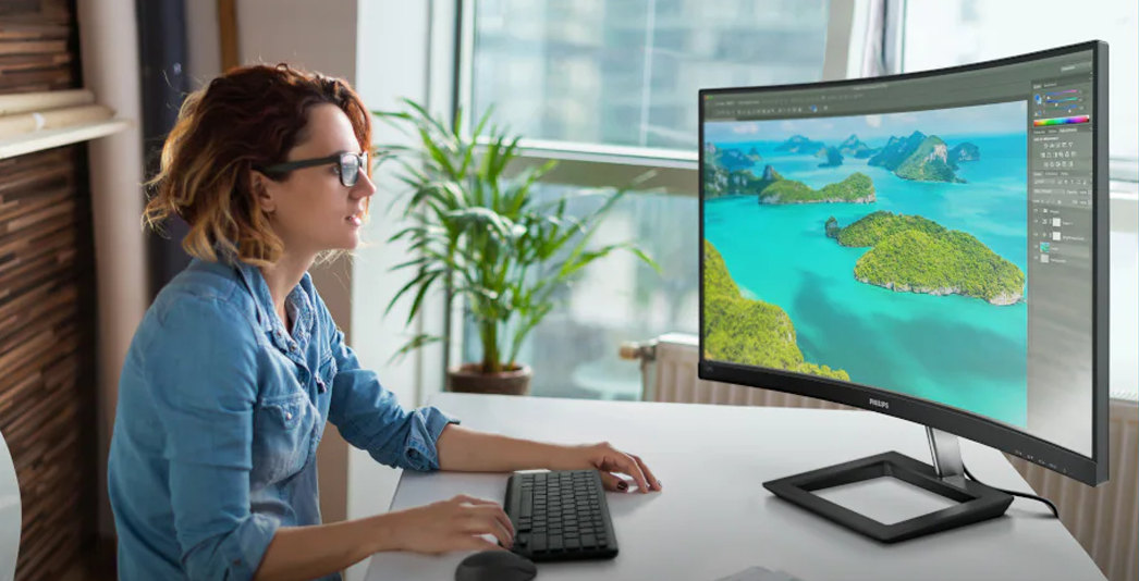Person sitting at a desk using a computer, with a large monitor displaying a tropical island landscape.