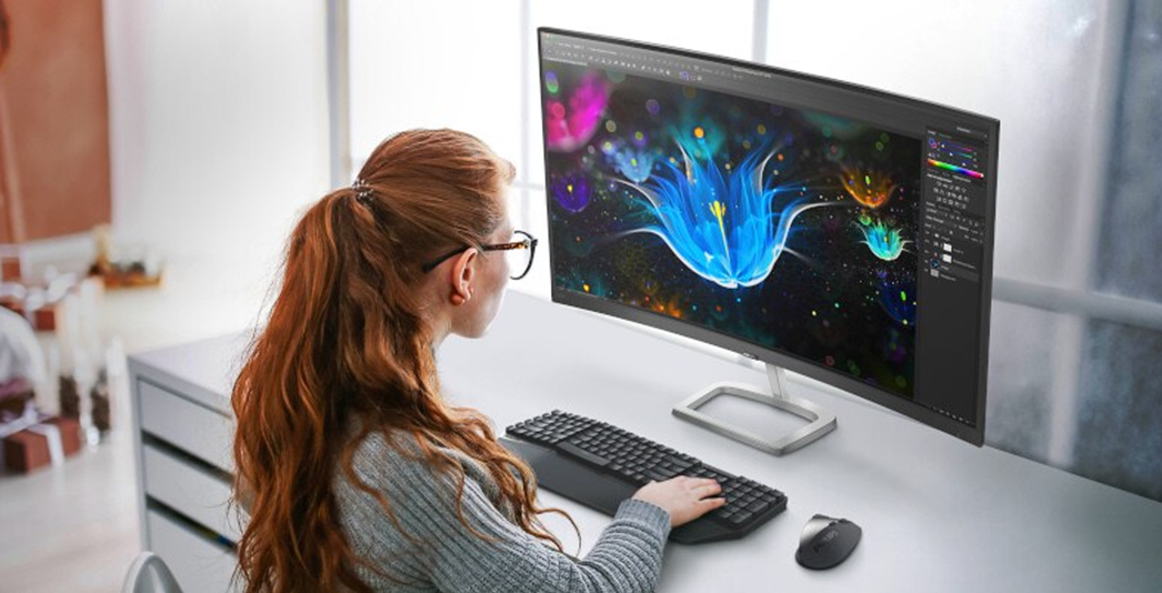 Person using a desktop computer with a wide monitor displaying colourful digital artwork.