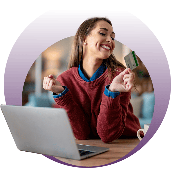 A person wearing a red sweater holding a credit card while using a laptop