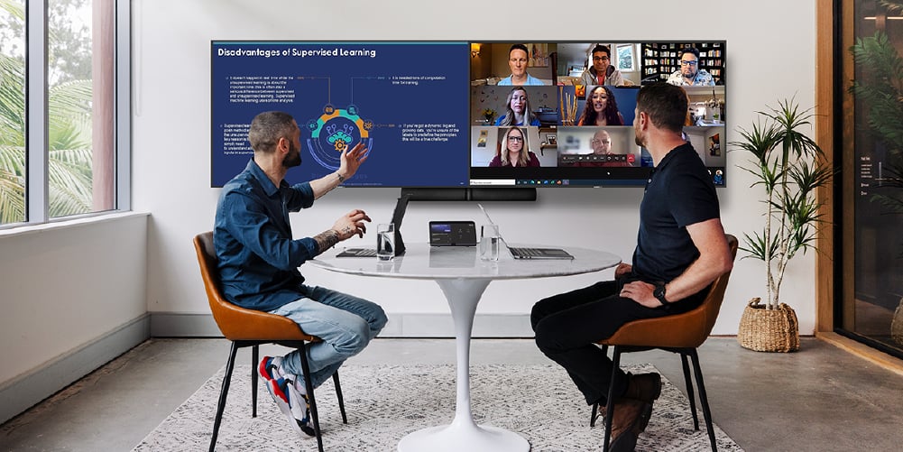 Two people in a meeting conference call facing a big double screen