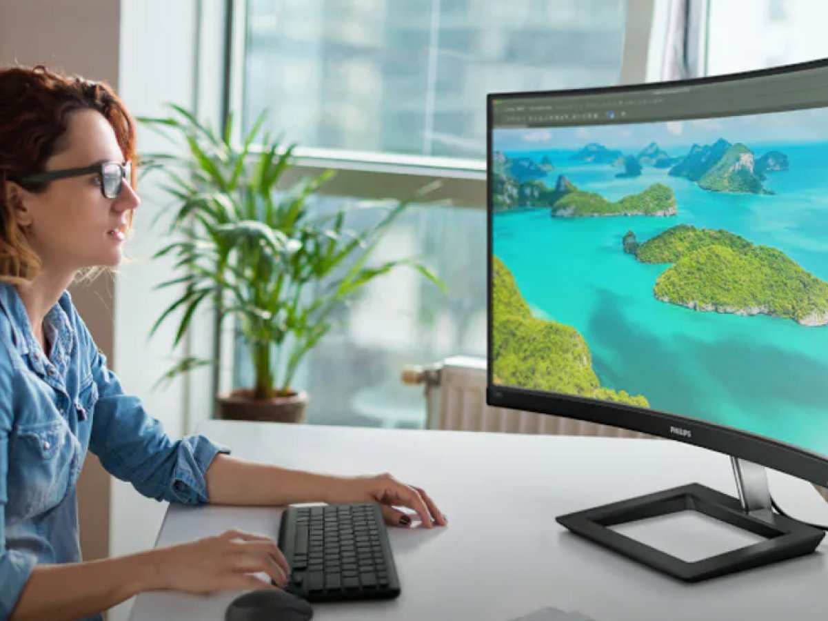Person sitting at a desk using a computer, with a large monitor displaying a tropical island landscape.