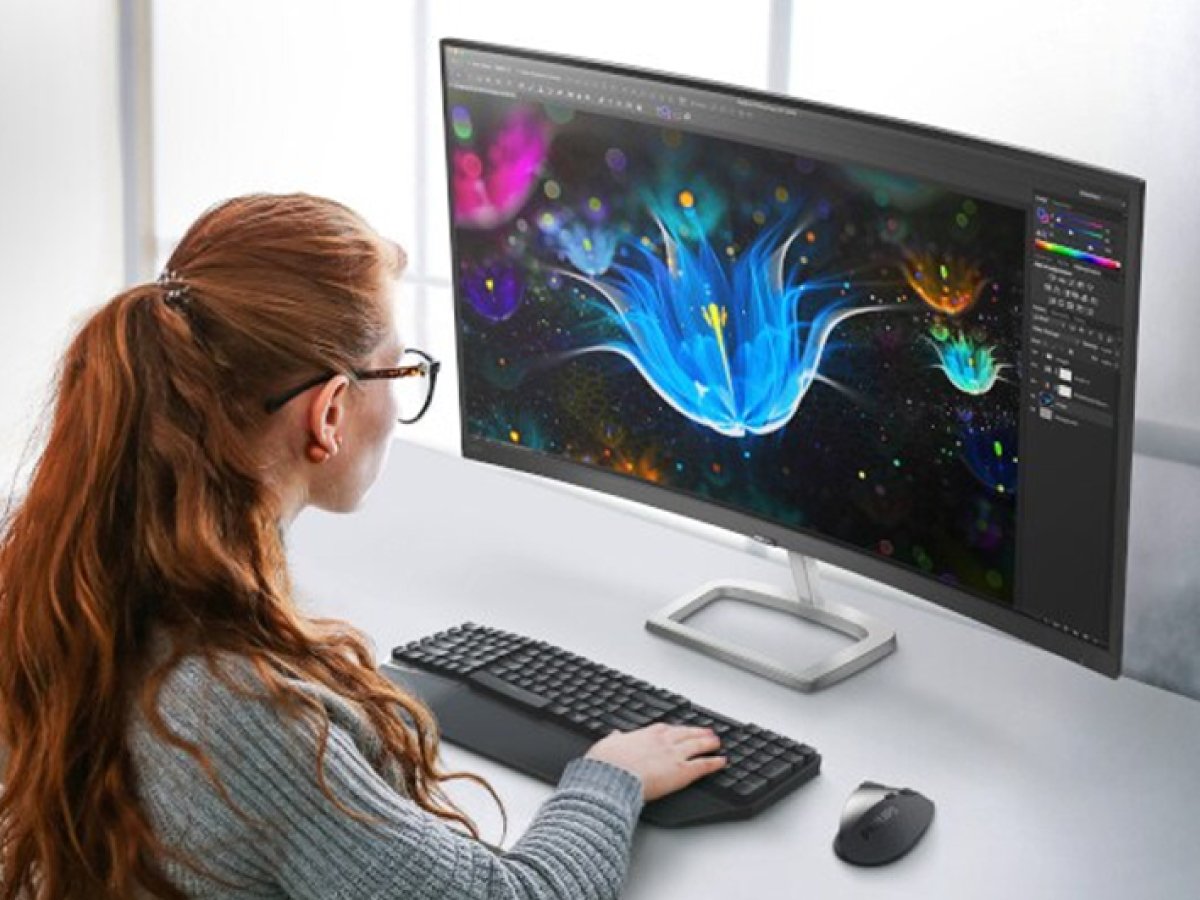 Person using a desktop computer with a wide monitor displaying colourful digital artwork.