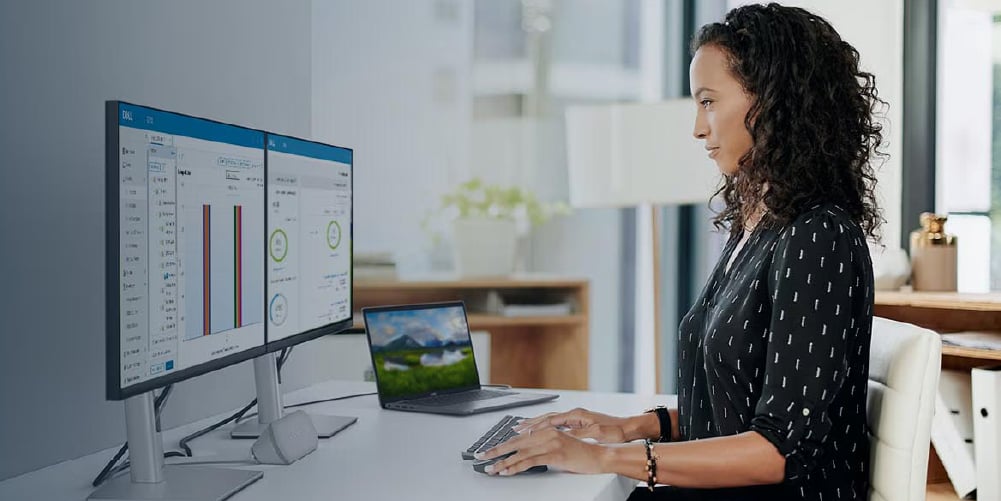 Person working at a desk looking at two Dell monitors plugged into a Dell laptop